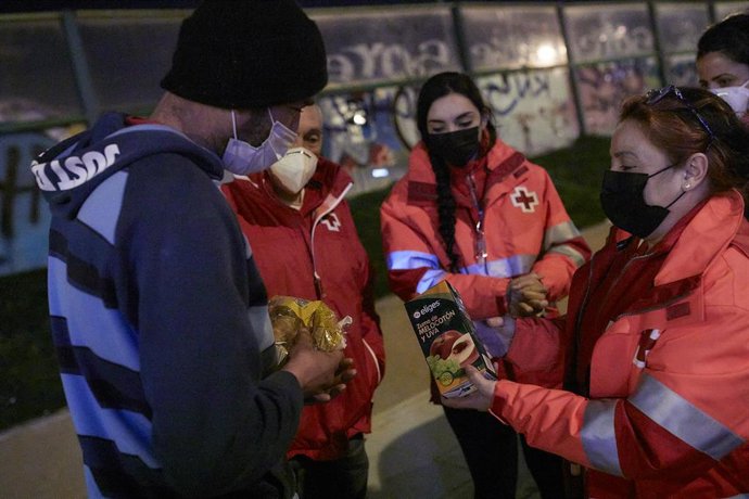 Archivo - Varios trabajadores de Cruz Roja ofrecen comida a un hombre sin hogar en el municipio madrileño de Getafe, Madrid.