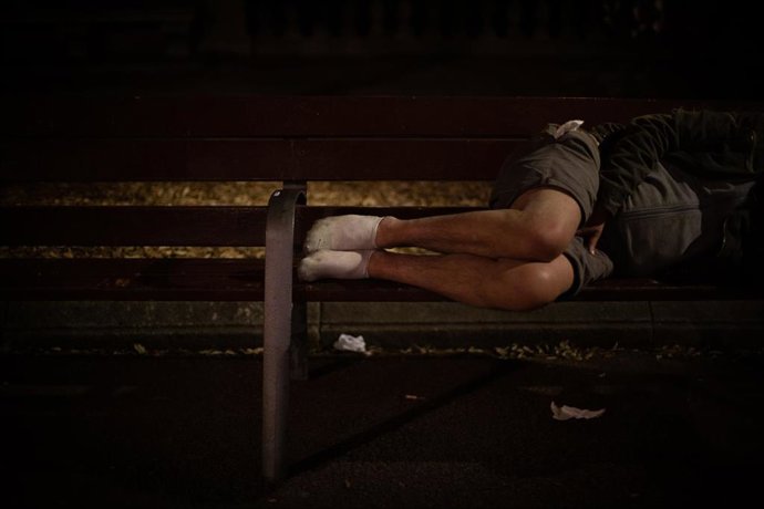 Archivo - Un hombre duerme sobre un banco en la Plaza de Catalunya, en Barcelona.