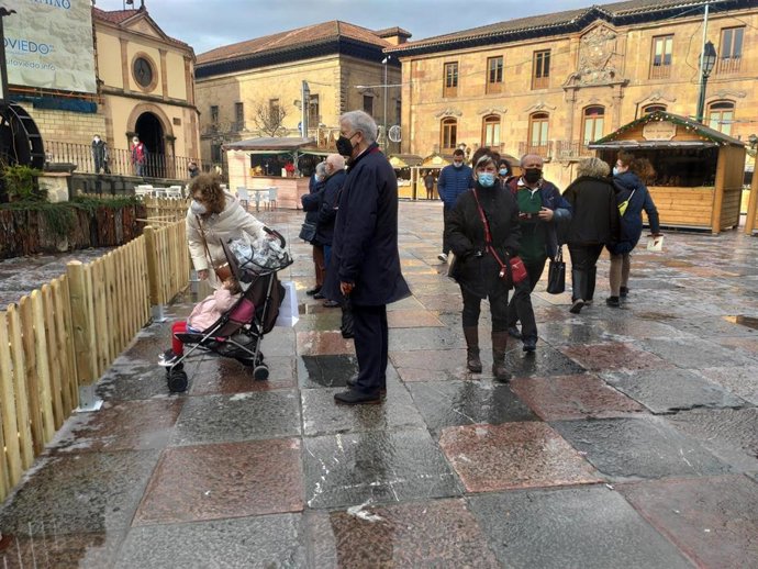 Personas paseando por la Plaza de la Catedral de Oviedo durante un día de otoño, con el Belén y las casetas del mercadillo navideño ya instaladas.