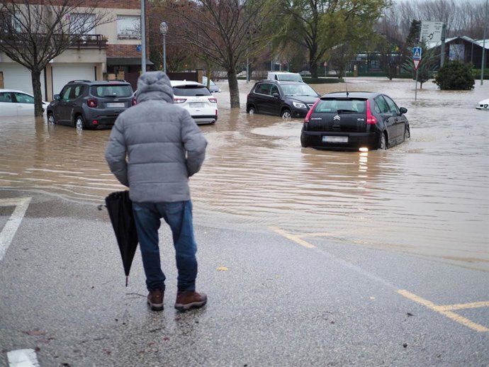 Una persona al lado de una vía llena de coches rodeados de agua, a 10 de diciembre de 2021, en Pamplona.