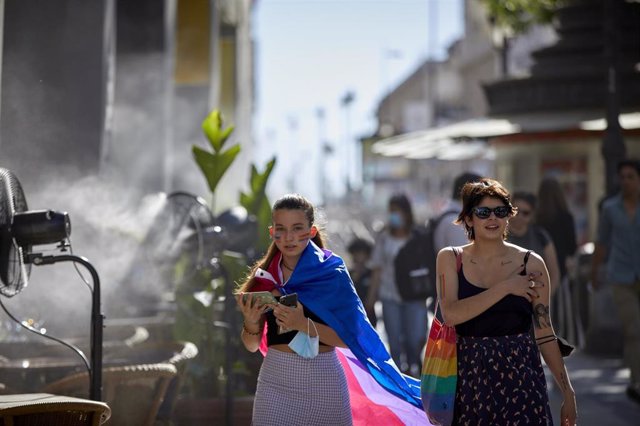 Archivo - Dos chicas con un bolso y una bandera LGTBI, al lado de un difusor de vapor de agua de un restaurante de la calle Alcalá, a 2 de julio de 2021, en Madrid, (España). 