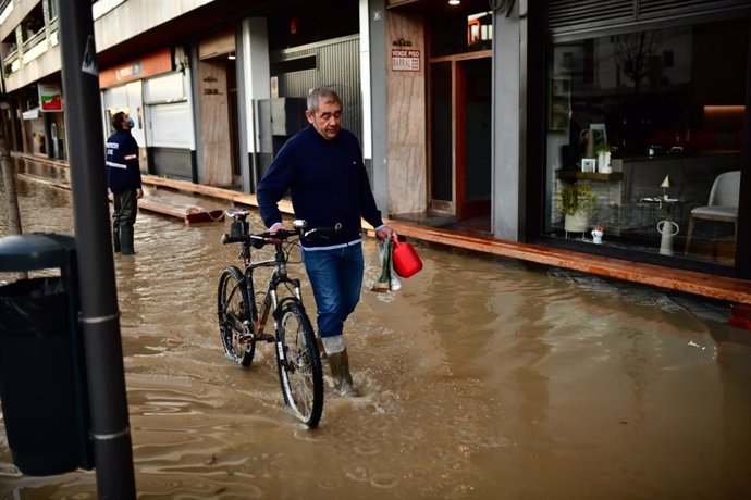 Un hombre pasa con su bicicleta por una calle inundada por la crecida del Ebro en Tudela