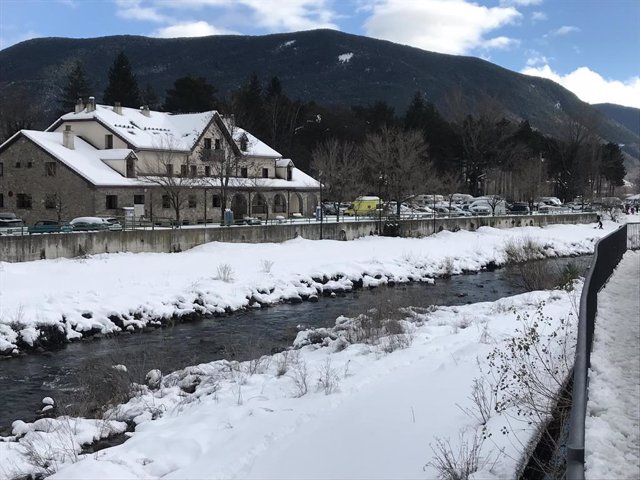 Río con nieve en las riberas y casa de montaña con tejado nevado