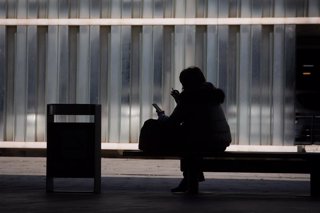 Una mujer mira su teléfono móvil sentada en un banco en el Aeropuerto de Barcelona-El Prat