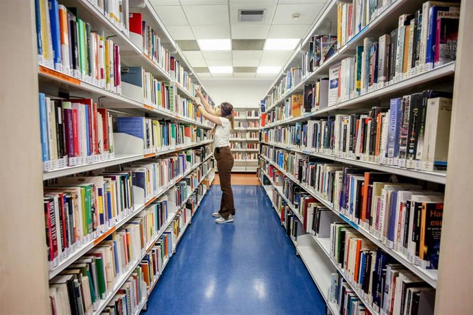Archivo - Una mujer en uno de los pasillos de libros de una biblioteca pública, en una foto de archivo.