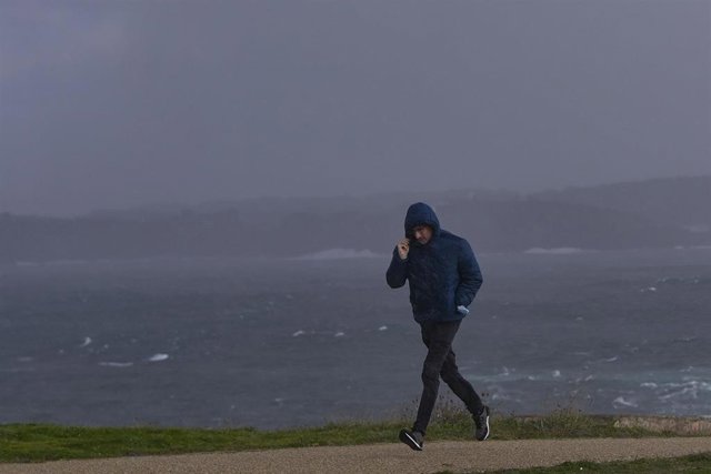Un hombre se protege del viento y la lluvia en la zona de la Torre de Hércules