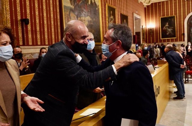 El todavía alcalde Juan Espadas saluda a Antonio Muñoz minutos antes de leer su renuncia al cargo en el Pleno extraordinario del Ayuntamiento de Sevilla.