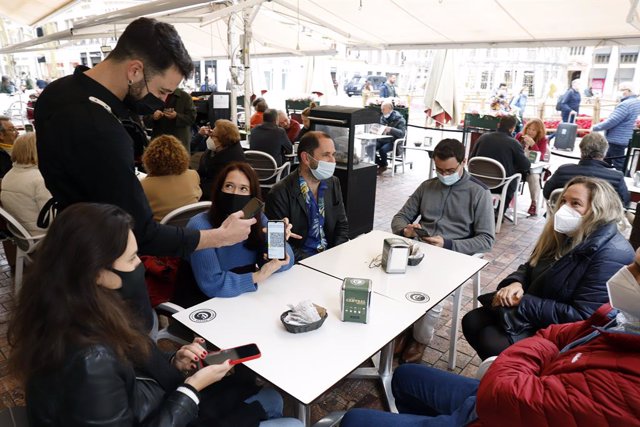 Un camarero pide certificado a los clientes en una mesa en la terraza de un bar durante el primer día de petición de Certificados Covid-19 para la hostelería, a 20 de diciembre de 2021 en Málaga (Andalucía, España)