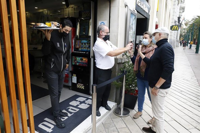 Un camarero pide certificado a los clientes en la puerta de un bar.