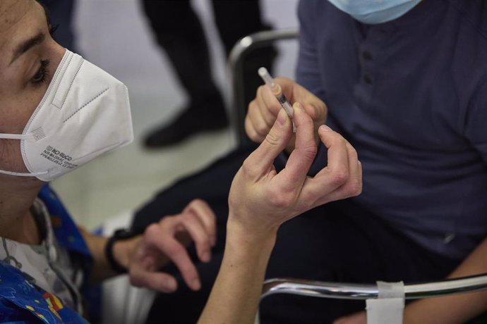 Una profesional sanitaria muestra a un niño una jeringuilla con una dosis de la vacuna contra el Covid-19, foto de recurso