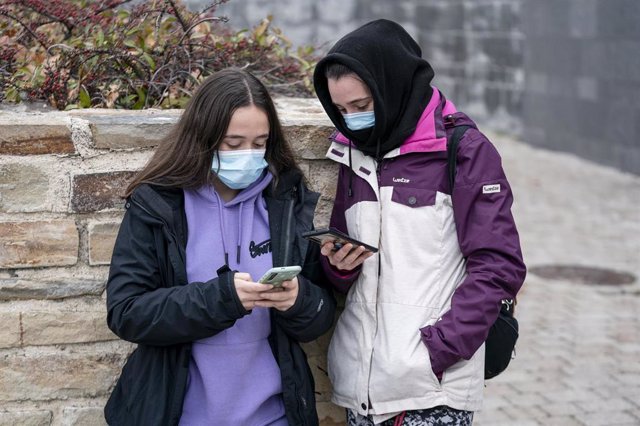 Dos chicas con mascarilla mirando sus móviles.