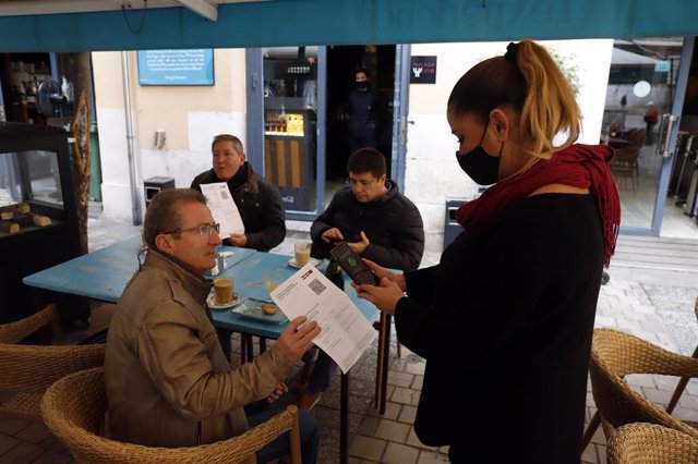 Una camarera pide certificado a los clientes en una mesa en la terraza de un bar durante el primer día de petición de Certificados Covid-19 para la hostelería, a 20 de diciembre de 2021 en Málaga (Andalucía, España)