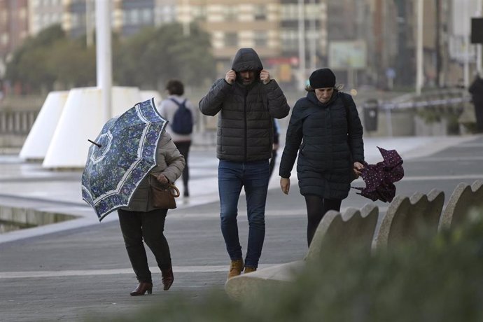 Tres personas con paraguas en el Paseo Marítimo de A Coruña donde se aprecia fuerte viento como consecuencia de la borrasca Barra, a 7 de diciembre de 2021, en A Coruña, Galicia (España). Galicia termina el puente de la Constitución en alerta naranja po