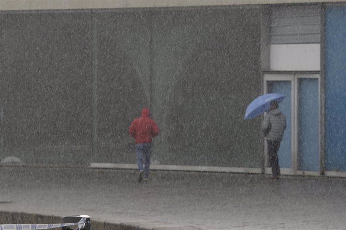 Dos personas caminan por el paseo marítimo mientras llueve, a 8 de diciembre de 2021, en A Coruña, Galicia, (España). La borrasca Barra ha hecho que la Xunta haya activado para todo el litoral gallego una alerta naranja por temporal costero. Según las p