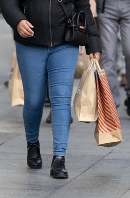 Archivo - Una mujer camina con bolsas con compras