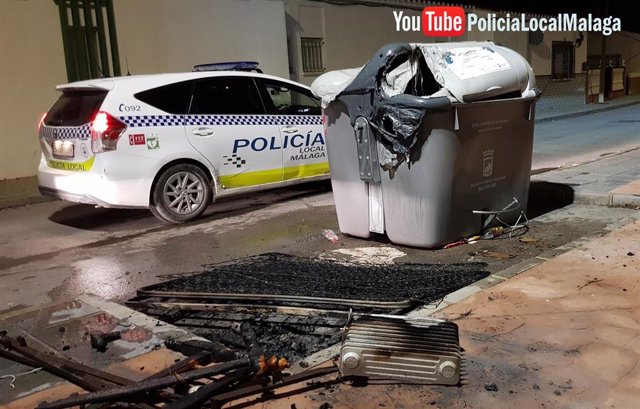 Un coche de la Policía Local de Málaga junto a un contenedor quemado y los restos de otro calcinado en la capital