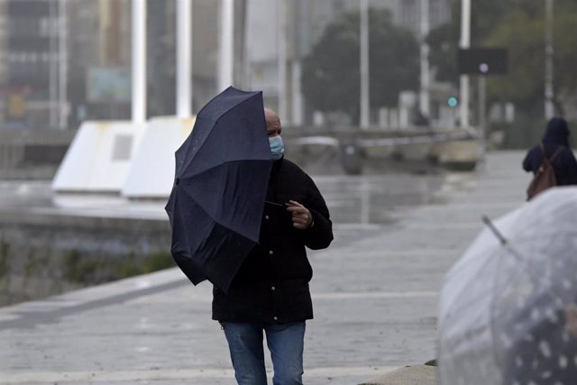 Un hombre con un paraguas camina por el paseo marítimo mientras llueve, a 8 de diciembre de 2021, en A Coruña, Galicia, (España). La borrasca Barra ha hecho que la Xunta haya activado para todo el litoral gallego una alerta naranja por temporal costero. S
