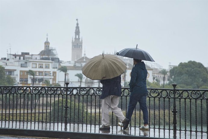 Archivo - Una pareja cruzando el Puente de Isabel II en un día lluvioso del puente de Todos los Santos el 30 de octubre de 2021 en Sevilla (Andalucía, España)