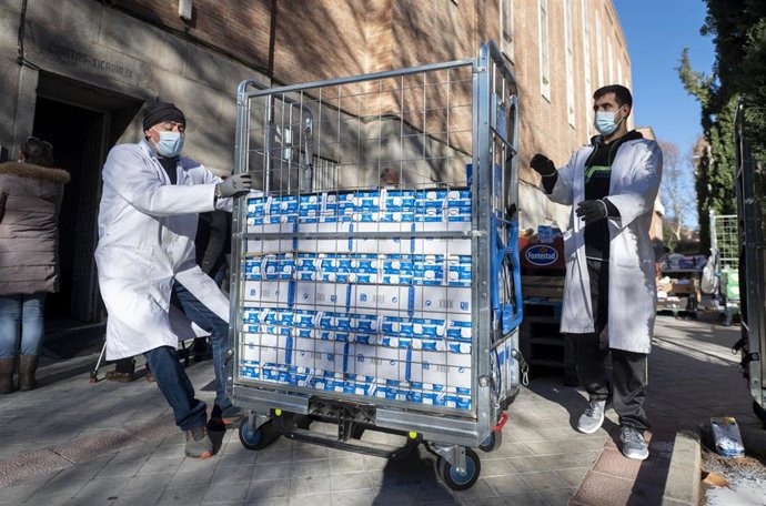 Dos personas llevan litros de leche en una entrega de alimentos organizada por la Fundación Madrina, a 30 de diciembre de 2021