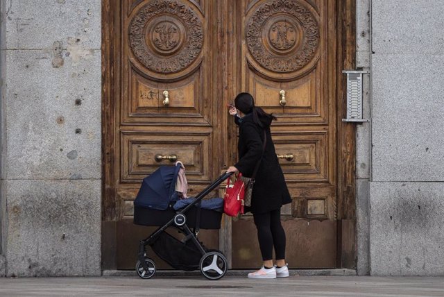 Archivo - Una mujer frente a un portal de la capital con un carrito de bebé.
