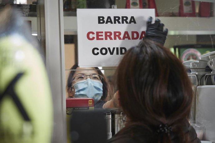 Un camarera coloca un cartel de barra cerrada por Covid.