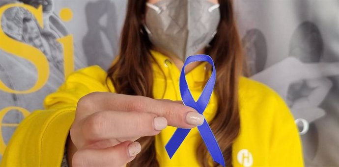 Una empleada de Hefame sostiene un lazo azul,  símbolo de la lucha contra el cáncer de colon