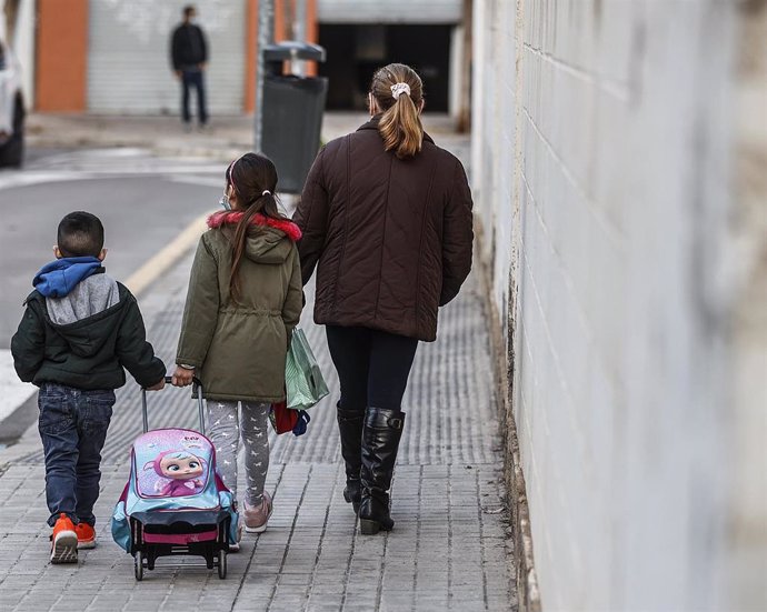 Un niño y una niña, acompañados de una mujer, caminan hacia el colegio, en Valencia.