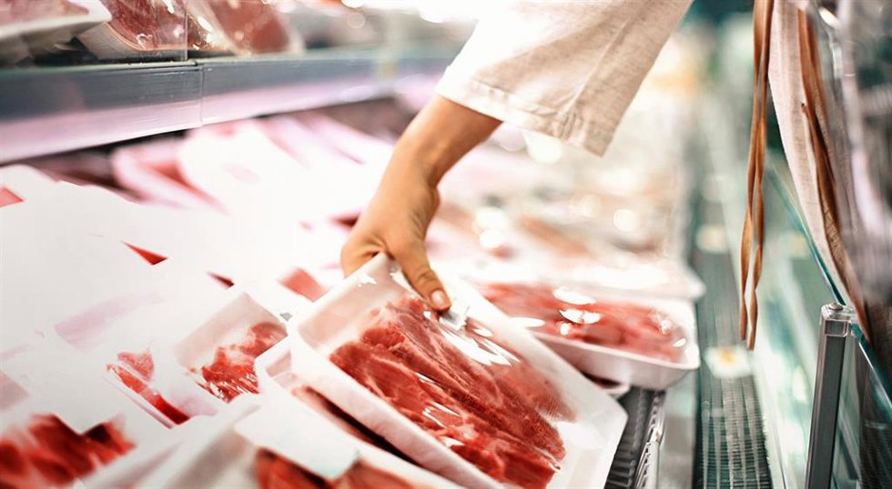 Una mujer sostiene una bandeja de carne en un supermercado.