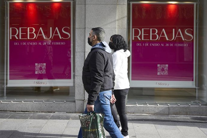 Dos personas pasan delante de una tienda con carteles de rebajas en una calle comercial del centro de Madrid, a 2 de enero de 2022, en Madrid, (España). Comienzan las rebajas de enero que generarán un 14 % más de empleo, sobre todo en logística, respect