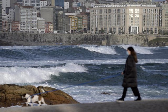 Archivo - Una mujer pasea a su perro en el Paseo Marítimo de A Coruña donde se aprecia fuerte oleaje.