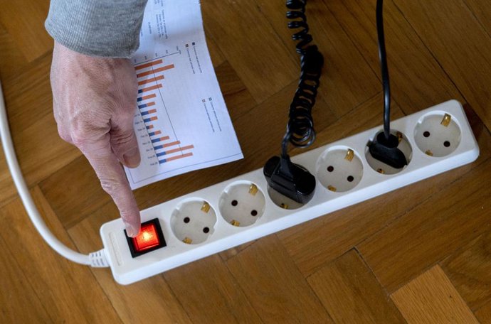 Un home encén una largadera amb diversos endolls amb una factura de llum a la m.