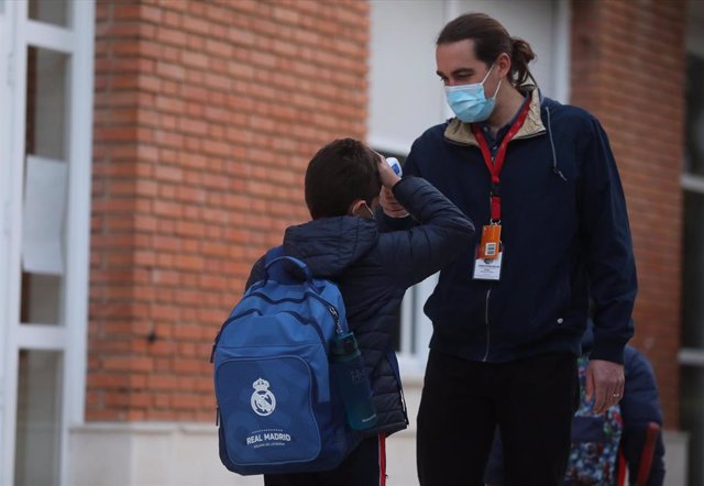 Un trabajador toma la temperatura a un niño a su llegada al primer día de clase presencial tras la Navidad, en el Colegio Privado Alameda de Osuna, a 10 de enero de 2022, en Madrid, (España)