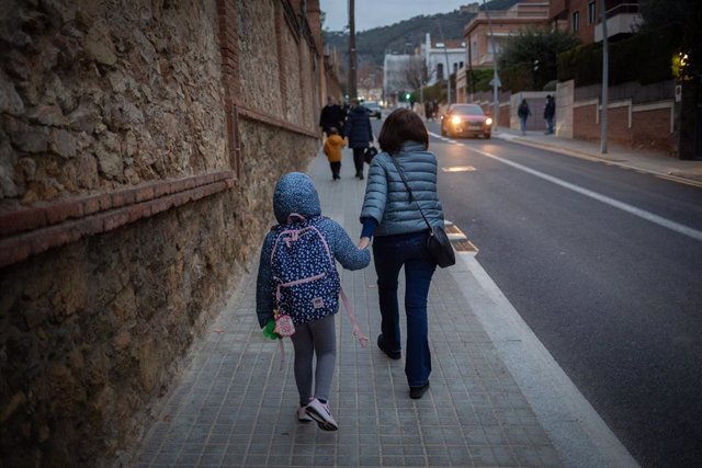 Una mujer lleva de la mano a un niño a su colegio