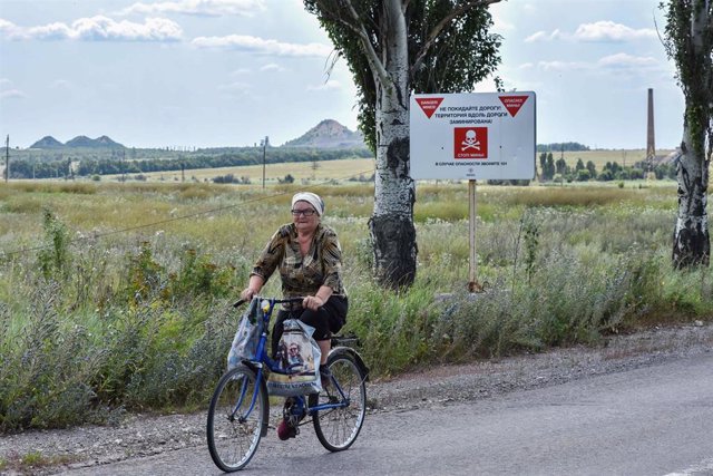 Archivo - Una mujer monta en bicicleta junto a un aviso de minas a las afueras de Krasnohorivka, en el Donbás