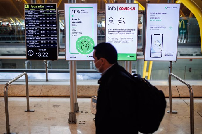 Una persona pasa delante de unos paneles con las medidas de seguridad Covid en la Terminal 4 del Aeropuerto Adolfo Suárez-Madrid Barajas, a 30 de diciembre de 2021, en Madrid, (España). A tan solo un día de Nochevieja, las estaciones de tren, avión y ca