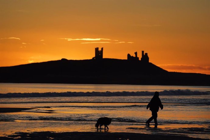 13 January 2022, United Kingdom, Alnwick: The sun rises over the ruins of Dunstanburgh castle on the Northumberland coastline. The 14th century castle is owned by the National Trust and managed by English Heritage. Photo: Owen Humphreys/PA Wire/dpa