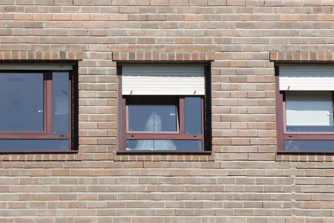 Archivo - Un trabajador sanitario con un EPI, en la ventana de una habitación de una residencia durante la pandemia.