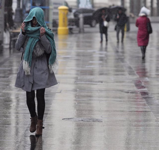 Archivo - Una mujer se tapa con una bufanda para refugiarse de la lluvia