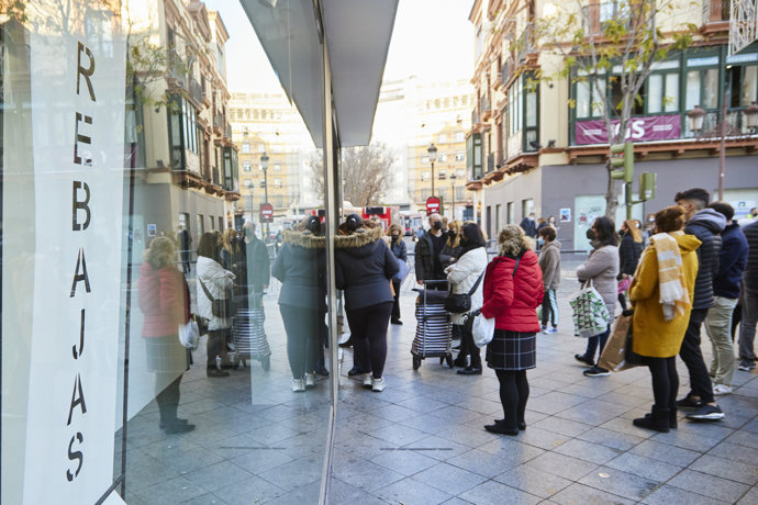 Detalle de un cartel de rebajas y varias personas esperando que abran los negocios durante el primer día de las rebajas, a 7 de enero de 2022 en Sevilla (Andalucía, España)
