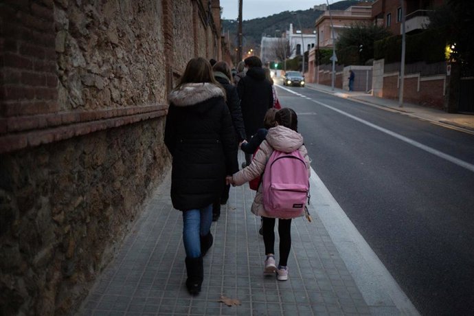 Una mujer lleva de la mano a un niño a clase
