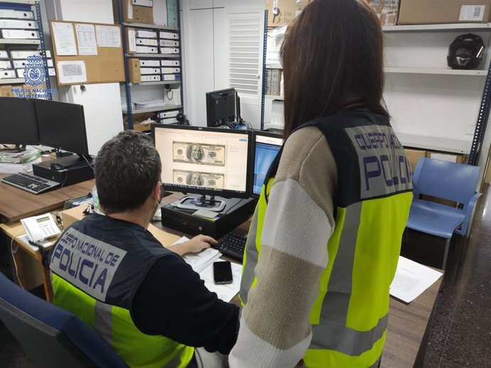 Agentes de la Policía Nacional en Palma observando los billetes de dólar falsos introducidos por el detenido.