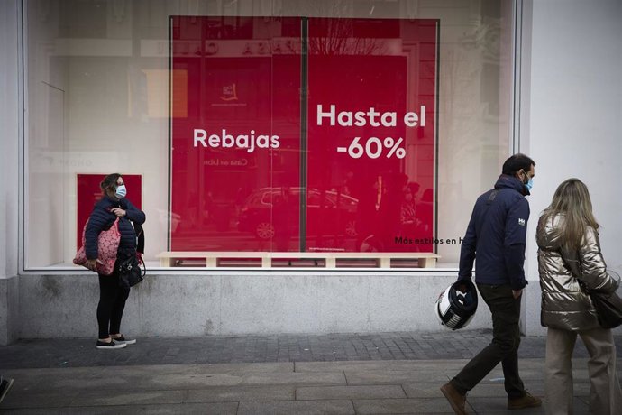 Varias personas pasan delante de un escaparate con cartel de rebajas en una calle comercial del centro de Madrid.