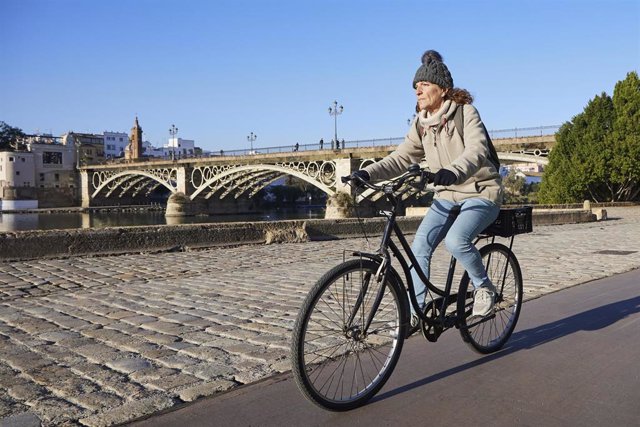 Archivo - Una ciclista, abrigada, durante el primer día de frío, a 23 de noviembre de 2021 en Puente de Triana en Sevilla (Andalucía, España)