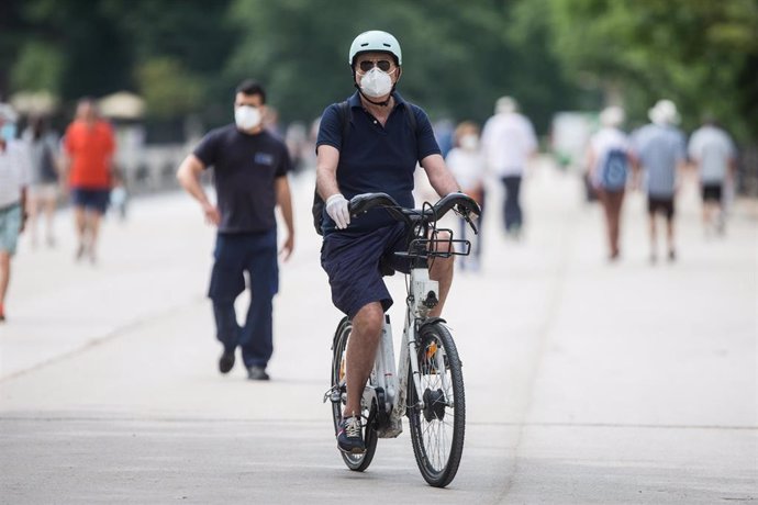 Archivo - Un hombre protegido con mascarilla y guantes monta en una bicicleta BiciMAD en el parque de El Retiro.