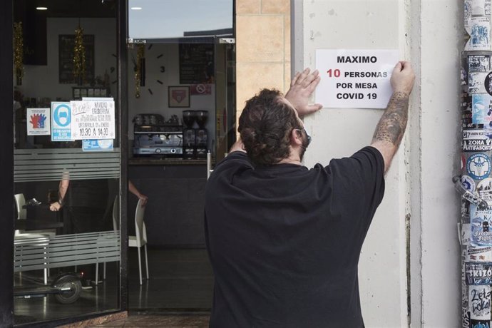 Archivo - Un camarero coloca un cartel de reducción de aforo por Covid en su local