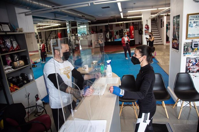 Archivo - Una clienta con mascarilla es atendida en la recepción de una escuela de boxeo