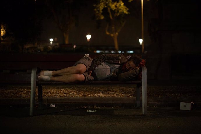 Archivo - Un hombre duerme sobre un banco en la Plaza de Cataluña.