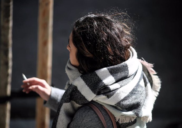 Archivo - Una mujer abrigada con bufanda y abrigo, fumando durnate un día de viento por Madrid (España), a 8 de noviembre de 2019.