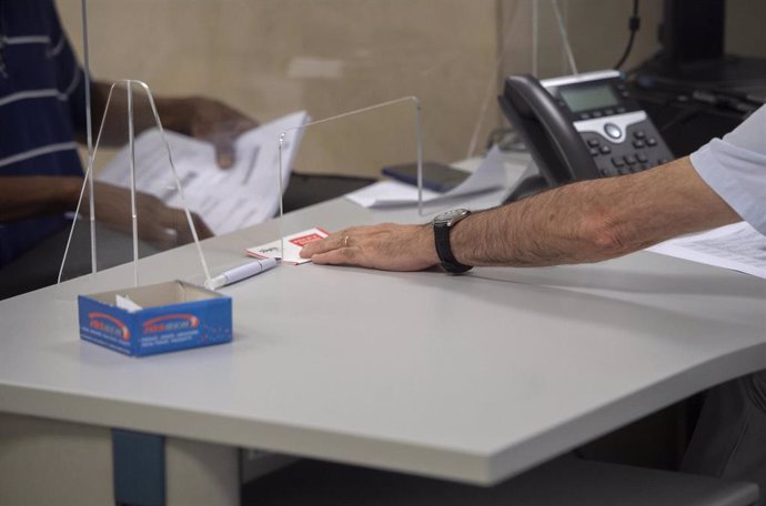 Archivo - Un empleado atiende a una persona en su puesto de trabajo de una oficina de Hacienda