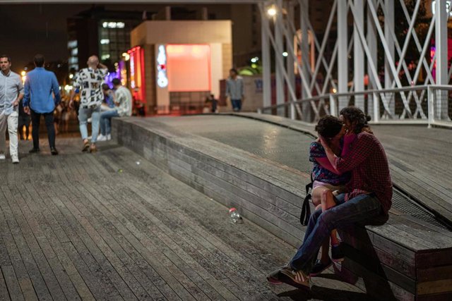 Archivo - Una pareja se besa, mientras los jóvenes que salen de fiesta pasan por su lado en Barcelona
